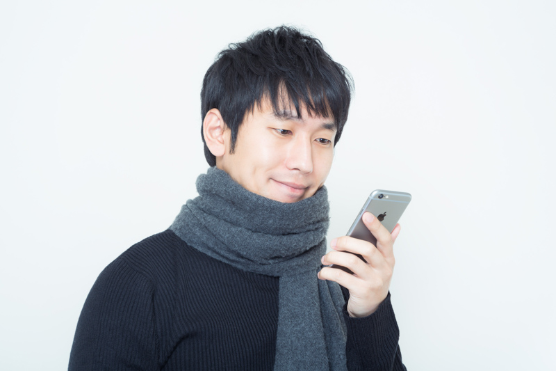 スマホを覗き微笑むマフラーを首に巻いた男性